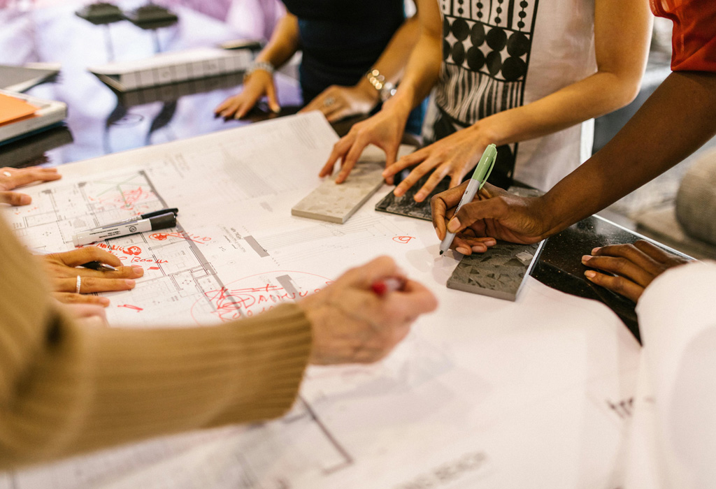 A diverse group of professionals collaborates over architectural plans and material samples, symbolizing teamwork and hands-on expertise in real estate development